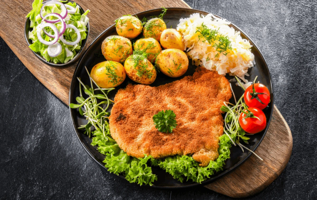 Kotlet schabowy z młodymi ziemniakami i surówkami na czarnym talerzu